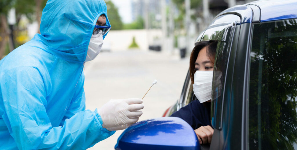 Nurse wearing PPE suit or Medical workers in full protective gear takes sample from woman driver inside the car. Drive-thru test for Coronavirus COVID-19